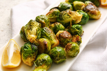 Plate with delicious roasted Brussels cabbage and lemon on table, closeup