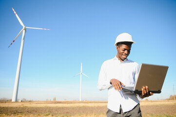African Engineer standing and hoding laptop with wind turbine