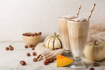 Glasses of tasty pumpkin latte on light background
