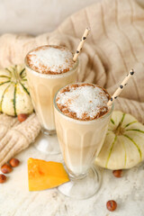 Glasses of tasty pumpkin latte on light background