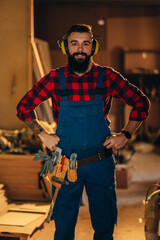 Young male carpenter working in workshop and wearing safety earphone
