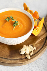 Wooden board with bowl of tasty pumpkin cream soup, and seeds on light background, closeup