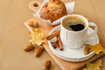 Cup of coffee with acorns, autumn leaves and cupcake on color wooden background