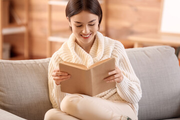 Beautiful young woman reading book on sofa at home