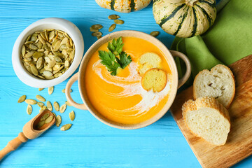 Pot with delicious pumpkin cream soup, seeds and croutons on color wooden background