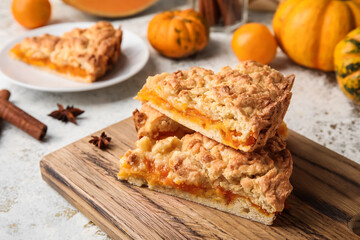 Wooden board with pieces of tasty pumpkin pie on light background