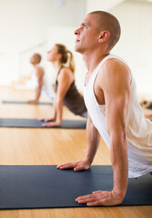 Adult man doing yoga with group of people in fitness studio, standing in stretching asana Urdhva Mukha Shvanasana known as Upward Facing Dog pose