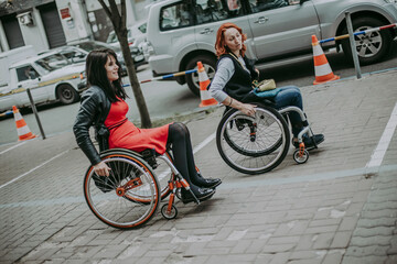 Fototapeta na wymiar Two girls in wheelchairs drive along road with cars in city. Girls travel to street accessible to people with special need in wheelchairs.
