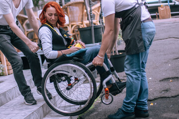 Waiters lift a girl in a wheelchair up the steps without a ramp. A woman is going to have lunch in a cafe inaccessible to people with special needs