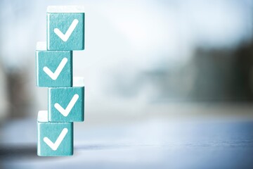 A white checkmarks on a stack of light blue toy blocks on table. Concept of questionary, checklist,