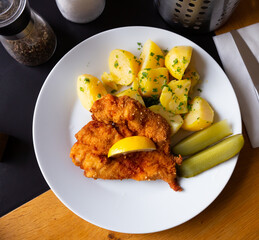 Top view of Parmesan breaded chicken schnitzel with garnish of boiled potatoes with fresh parsley...