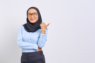 Portrait of smiling young Asian woman pointing thumbs at copy space isolated on white background