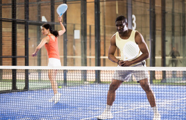 Focused African American playing friendly paddleball match on small closed court. Concept of concentration in competition.