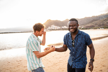 Two handsome multiethnic male friends having a good time together at the beach, smiling, talking,...
