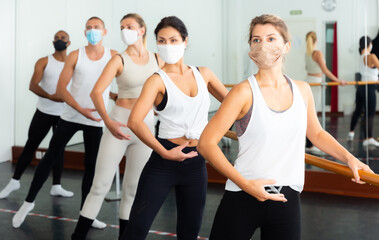 Fototapeta na wymiar Group of men and women in protective masks practicing at the ballet barre