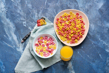 Bowls with colorful cereal rings and glass of juice on color background