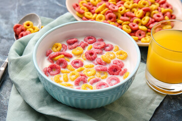 Bowls with colorful cereal rings and glass of juice on color background