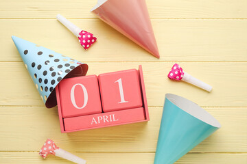 Calendar with date of April Fools Day, party hats and whistles on color wooden background