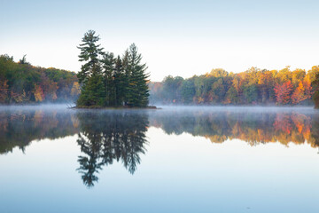 Beautiful calm lake with trees in autumn color and a small island in northern Minnesota at dawn - obrazy, fototapety, plakaty