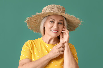 Portrait of beautiful mature woman in straw hat with hands near face on green background