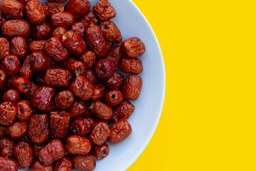 Dried Chinese jujubes in white plate on yellow background.