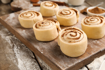 Board with uncooked cinnamon rolls on wooden background, closeup