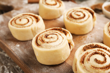Board with uncooked cinnamon rolls on wooden background, closeup