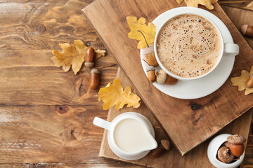 Cup of coffee with acorns, autumn leaves and milk on wooden background