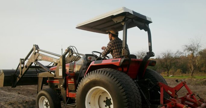 A male tractor driver drives an agricultural tractor plowing a small field