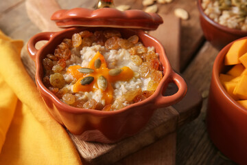 Pot of tasty oatmeal with pumpkin and raisin on wooden background