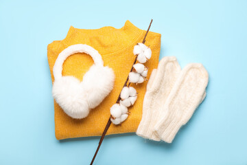 Knitted mittens, earmuffs, sweater and cotton branch on color background