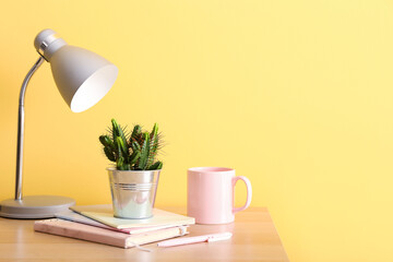 Green cactus, notebooks, lamp and cup on table against color wall