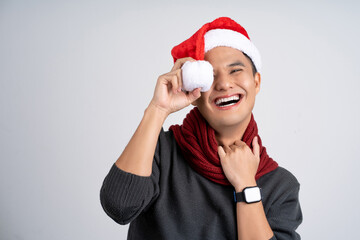 A charming photo of a smiling Asian man wearing a Christmas hat. hand holding a red scarf, isolated on a blue background.