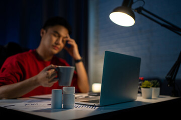 Young Asian businessman feeling stressed and tired after working long hours at night on his PC,...