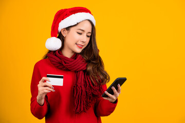 Pretty young asian woman in red sweater, hat isolated on yellow wall background, studio portrait. Healthy fashion lifestyle. She holding mobile phone, credit bank card