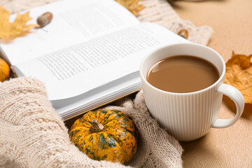 Cup of tasty coffee, book and autumn decor on beige background