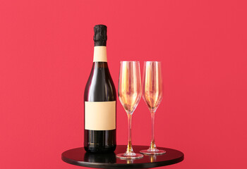 Bottle of champagne and glasses on dark table near color wall