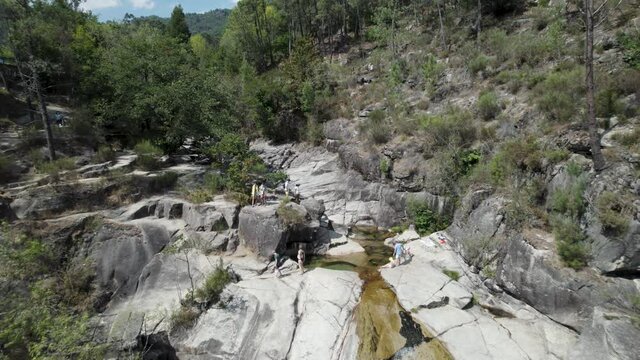 Drone flying over people relaxing on rocks of Cascatas de Fecha de Barjas in Peneda-Geres National park, Portugal. Aerial reverse