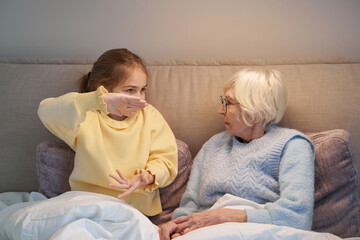 Serious grandmother playing charades with her granddaughter in bed