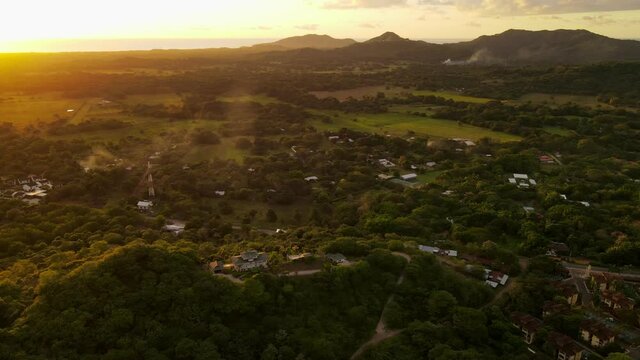 Cinematic aerial footage of a pompous mansion on a hill within the rainforest. Golden glow of the sunset above the pacific ocean covers everything in warm and soft tones.
