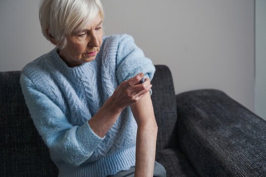 Elderly woman holding a syringe next to her shoulder