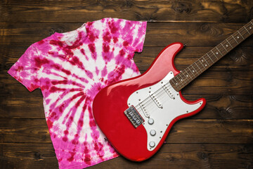 A red and white electric guitar and a red and white tie dye T-shirt on a dark wooden background....