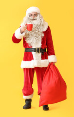 Santa Claus with cup of hot cocoa and bag on yellow background