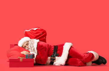 Santa Claus with bags and presents sleeping on red background
