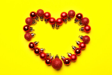 Heart made of red Christmas balls on yellow background