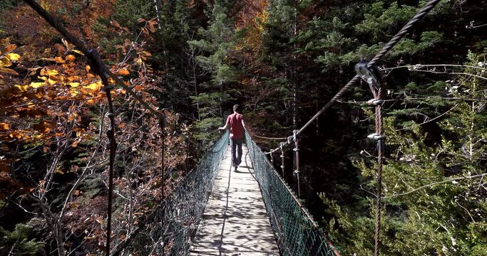 Back view of Young european hiker with red shirt  crossing suspension Bridge in spanish pyrenees in autumn