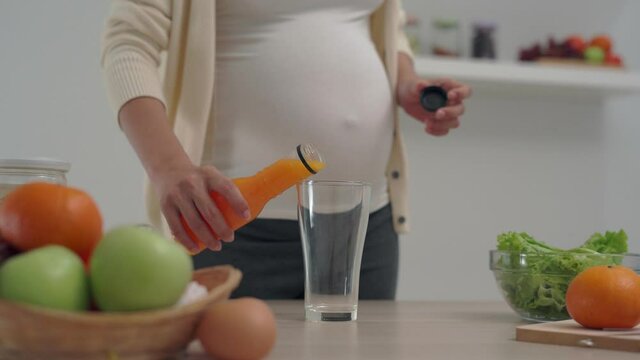 28 week pregnant woman holds an orange juice and chooses a nutritious diet for the healthy development and growth of her unborn child. happy and relax at home