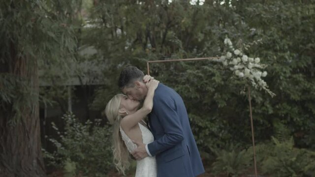 A married wedding couple embracing, hugging, and kissing in an wooded outdoor area.