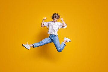 Obraz premium Woman in casual jeans clothes jumping with raised hands and legs isolated on yellow background. Winner