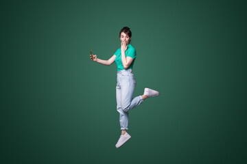 Fototapeta na wymiar Full length profile photo of shocked woman jumping high up hold telephone while looking at camera isolated over green color background